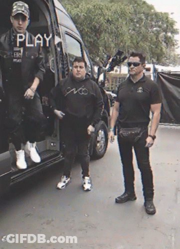 Two Men Standing In Front Of A Van With The Word Play On The Screen GIF