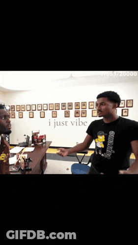 Two Men Standing In Front Of A Wall That Says I Just Vibe On It GIF