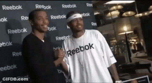 Two Men Standing In Front Of A Wall That Says Reebok On It GIF
