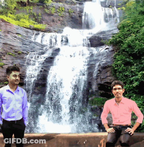 Two Men Standing In Front Of A Waterfall With One Wearing A Pink Shirt GIF