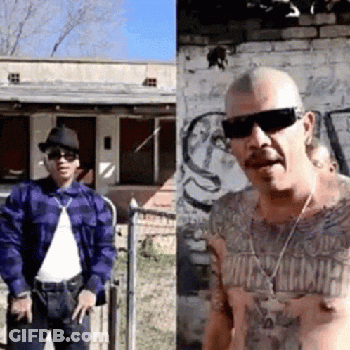 Two Men Standing In Front Of Brick Building GIF