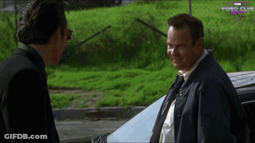 Two Men Standing In Front Of Car With Video Club GIF