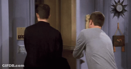 Two Men Standing In Front Of Door With Clock GIF
