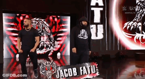Two Men Standing In Front Of Jacob Tatu Sign GIF