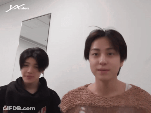 Two Men Standing In Front Of JX Labels Wall GIF