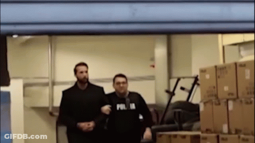 Two Men Standing In Room With Boxes, One Wearing Polis Shirt GIF