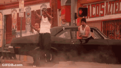 Two Men Standing Next To Car In Front Of Taco Store GIF