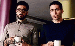 Two Men Standing Next To Each Other Holding Cups Of Coffee . GIF