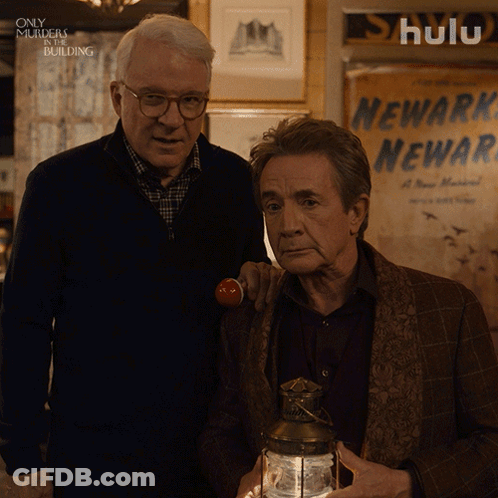 Two Men Standing Next To Each Other In Front Of A Sign That Says Newark Newark GIF