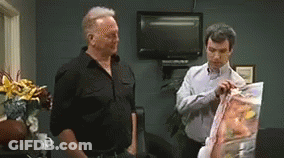 Two Men Standing Next To Each Other Looking At Bag Of Chips GIF