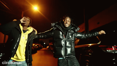 Two Men Standing Next To Each Other On A Street At Night GIF