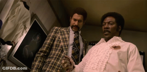 Two Men Standing Next To Each Other With One Wearing A White Shirt With Ruffles On The Sleeves GIF