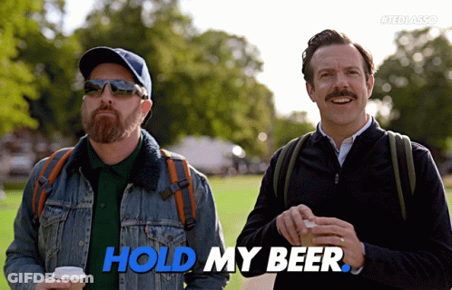 Two Men Standing Next To Each Other With The Words Hold My Beer In Blue GIF