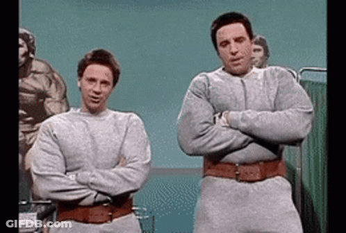 Two Men Standing Next To Each Other With Their Arms Crossed In A Hospital Room GIF