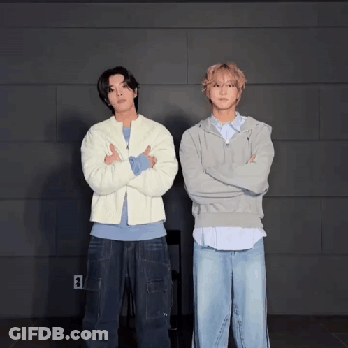 Two Men Standing Next To Each Other With Their Arms Crossed In Front Of A Wall With The Letter B On It GIF