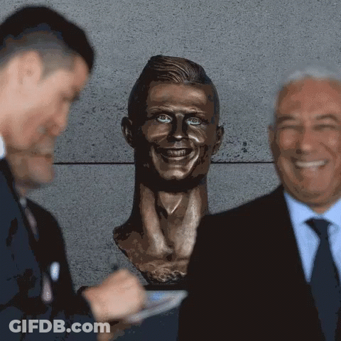 Two Men Standing Next To Man's Head Statue GIF