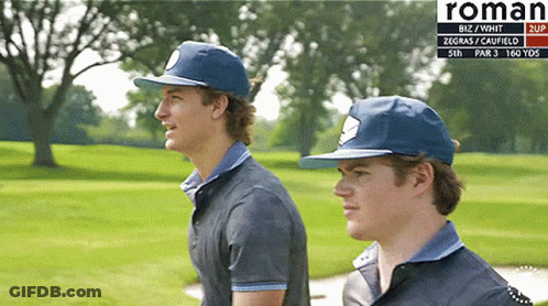 Two Men Standing On A Golf Course With Roman Written On The Bottom Right GIF