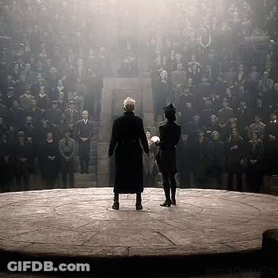 Two Men Standing On A Stage Holding Hands In Front Of A Large Crowd GIF