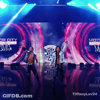 Two Men Standing On A Stage In Front Of A Screen That Says Top City GIF