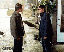 Two Men Standing On Sidewalk In Front Of Building GIF