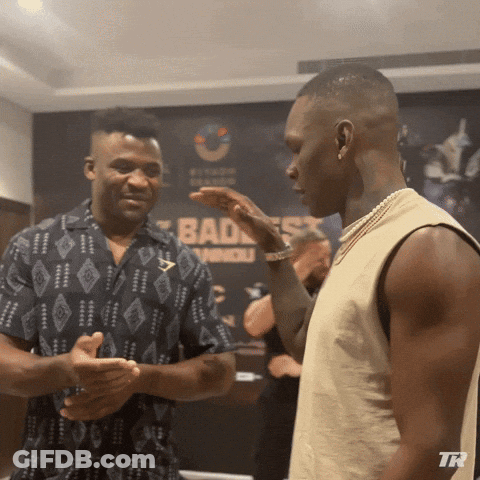 Two Men Talking In Front Of Bad Ass Sign GIF