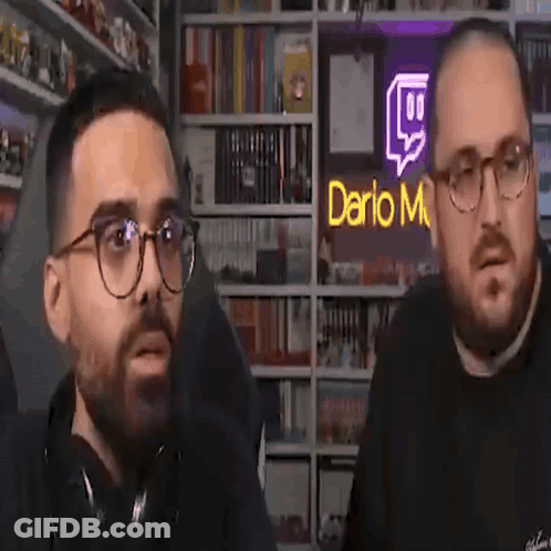 Two Men Talking In Front Of Dario M Sign GIF