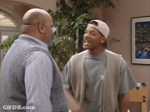 Two Men Talking In Living Room, One Wearing Hat GIF