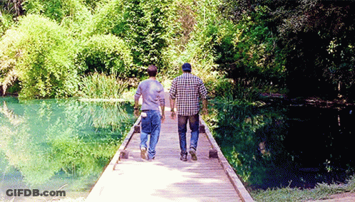 Two Men Walking Across Wooden Bridge Over River GIF