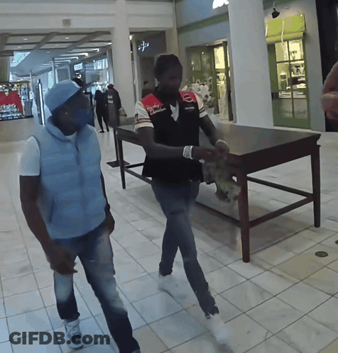 Two Men Walking In A Mall With One Wearing A Shirt That Says ' Columbia ' On It GIF