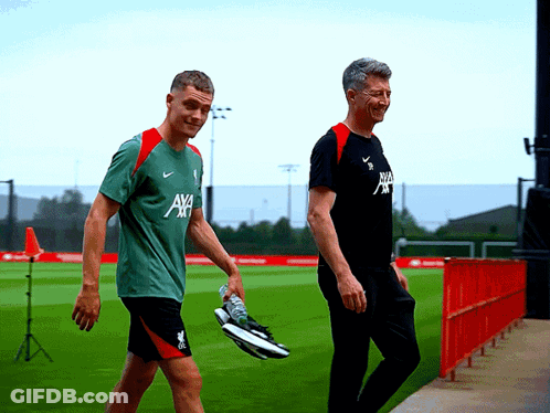 Two Men Walking On Field, One Wearing AXA Shirt GIF