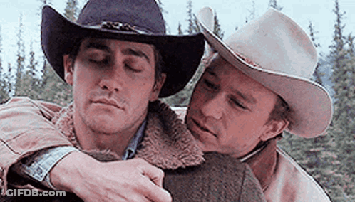 Two Men Wearing Cowboy Hats Are Hugging Each Other In A Forest . GIF