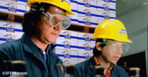 Two Men Wearing Hard Hats And Goggles Are Working In A Warehouse With Boxes Behind Them GIF
