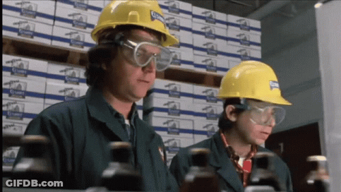 Two Men Wearing Hard Hats And Safety Goggles Are Looking At Bottles In A Warehouse With Boxes Of Clampy In The Backgroun GIF