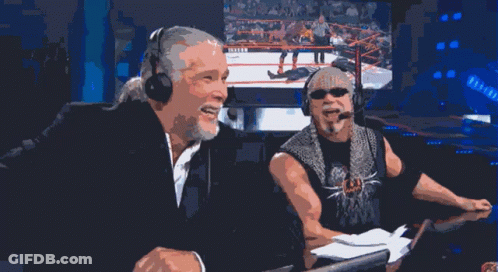 Two Men Wearing Headphones Are Laughing In Front Of A Screen With A Wrestling Match On It GIF