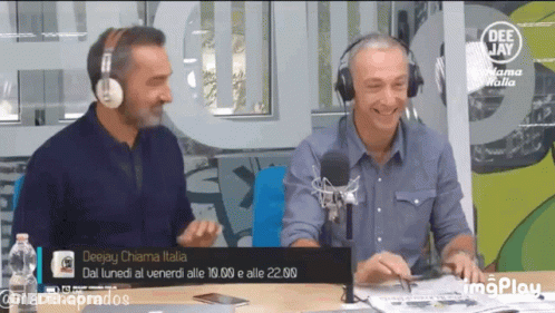 Two Men Wearing Headphones Are Sitting At A Table In Front Of A Deejay Chiama Italia Sign GIF