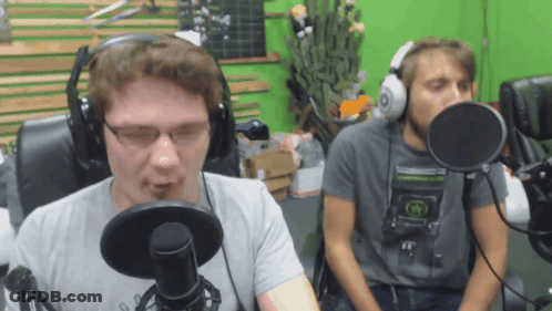 Two Men Wearing Headphones Are Talking Into Microphones In Front Of A Green Screen GIF