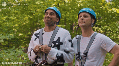 Two Men Wearing Helmets And Safety Harnesses Are Standing Next To Each Other In The Woods . GIF