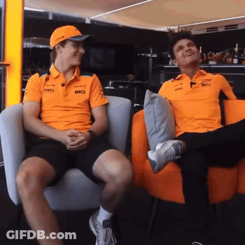 Two Men Wearing Orange Shirts Are Sitting In Chairs And Talking . GIF