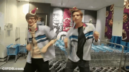 Two Men Wearing Santa Hats Dancing In Front Of Sign Albert Blitzman GIF