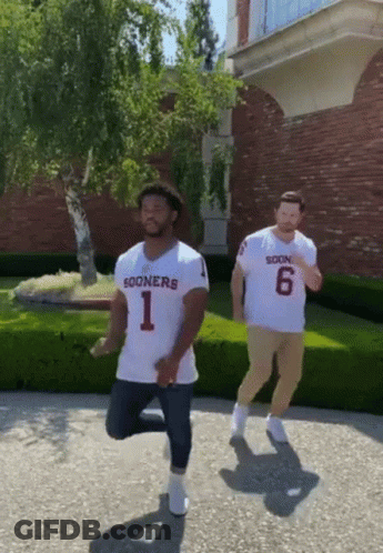 Two Men Wearing Sooners Jerseys Are Dancing On The Sidewalk GIF