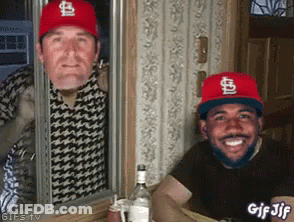 Two Men Wearing St Louis Cardinals Hats Are Looking Out Of A Window GIF