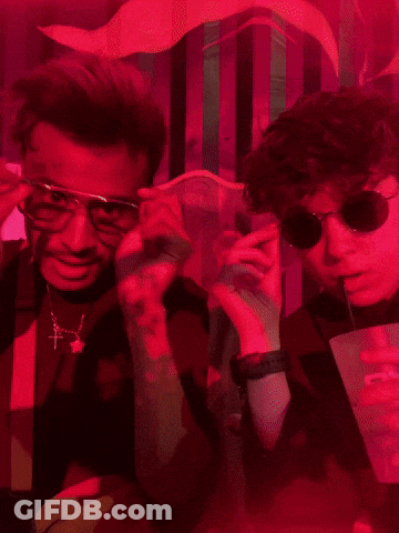 Two Men Wearing Sunglasses And Suspenders Pose For A Picture In A Dark Room GIF