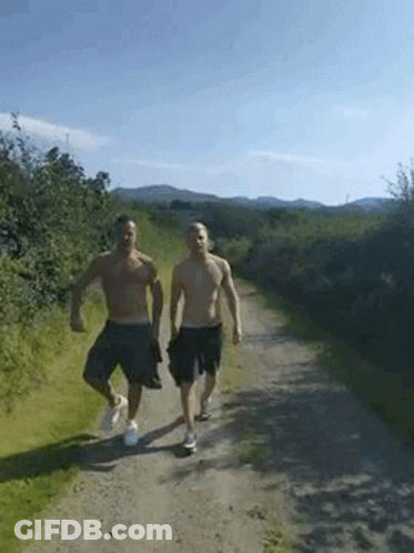 Two Men Without Shirts Are Walking Down A Dirt Road . GIF
