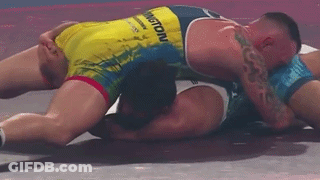 Two Men Wrestling On Mat One Laying On Ground GIF