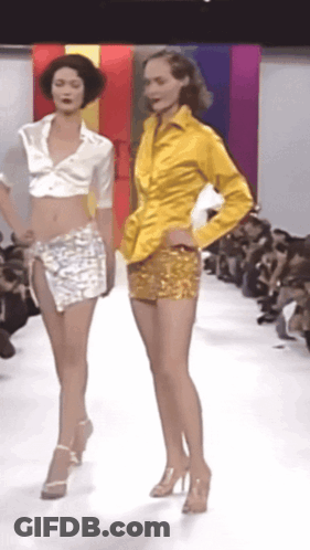 Two Models Are Walking Down A Runway Wearing Shorts And A Yellow Shirt GIF