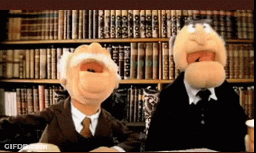 Two Muppets Are Sitting In Front Of A Bookshelf With Books On It GIF