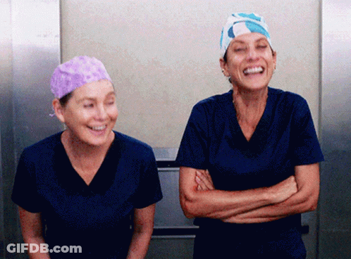 Two Nurses Wearing Scrubs And Hats Are Laughing Together GIF