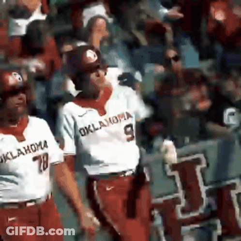 Two Oklahoma Baseball Players Are Walking In Front Of The Crowd GIF