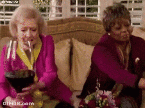 Two Older Women Are Sitting On A Couch Drinking Wine And Smoking Cigarettes . GIF