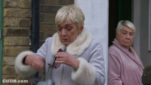 Two Older Women Are Standing Next To Each Other In Front Of A Brick Building . GIF